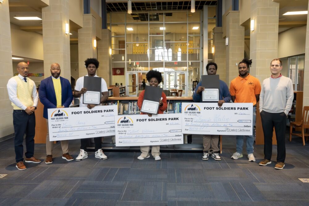 Students and educators posing for a photo, holding large checks showing awards.